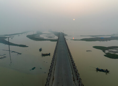 Aerial view of an empty road during a foggy day crossing a flooded field near Sapahar, Bangladesh.
