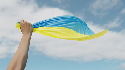 Ukrainian flag in hand on blue sky background