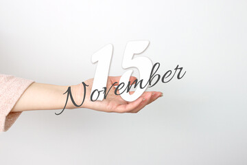 November 15th. Day 15 of month, Calendar date. Calendar Date floating over female hand on grey...