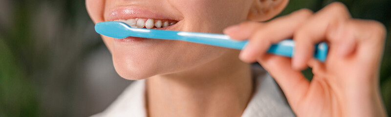 Closeup of young woman in white bathrobe brushing her teeth while standing in front of a mirror. Dental health care concept