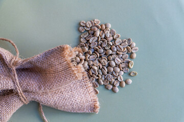 Raw coffee beans lies on green background next to brown sackcloth sack. Selective focus. Close-up...