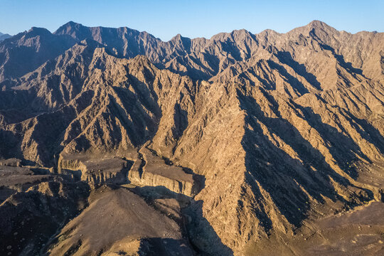 Aerial view of a canyon among the rocky and dry mountains in the desert in Ajman State, United Arab Emirates.