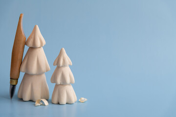 Handmade wooden carved Christmas trees with few shavings and carving knife stands on blue...