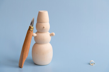 Carved wooden snowman and carving knife stands on blue background. Few wooden shavings on the...