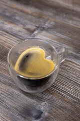 Double wall glass mug with fresh Caffè Americano stands on wooden table. Heart shaped coffee surface covered with crema. Copy space for your text. Romantic drink theme.
