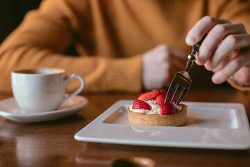 Close-up of unrecognizable person sitting at table and enjoying a delicious strawberry tart.