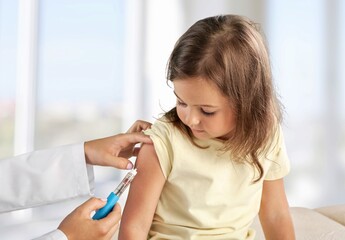 Female nurse giving an arm injection to a child. Little kid in getting a shot at a modern vaccination center. Covid 19 vaccine to a little girl - obrazy, fototapety, plakaty