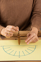 Top view of woman's hands holding a wooden pendulum over an energy diagram, on wooden table,...