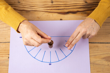 Top view of woman's hands holding a wooden pendulum over a yellow energy diagram, on wooden table,...