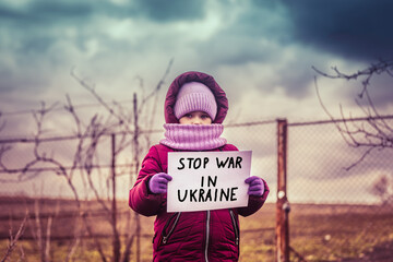 Little refugee girl with a sad look and a poster that says stop war in Ukraine. Social problem of...