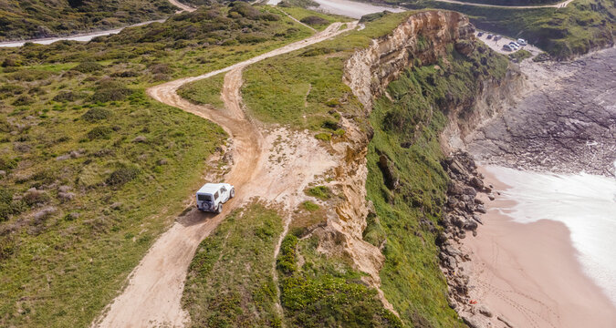 Aerial view of a four wheel drive car parked on the top of the cliff facing the Atlantic Ocean, Setubal, Portugal.