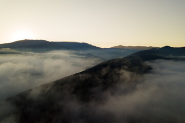 Aerial view of vibrant sunrise over white dense fog with distant dark silhouettes of mountain hills on horizon