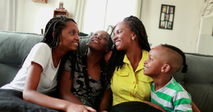 African mother and children sitting at home couch smiling, real people