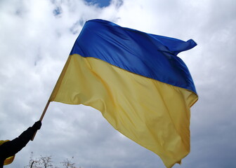 Fototapeta premium Flag of Ukraine in person's hand waves on wind against sky