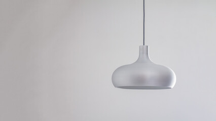 A silver metal lamp in a simple semicircular shape hangs on the ceiling against a gray wall...