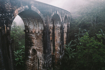 Aerial view of famous Nine arch railway bridge going through green jungle landscape in morning mist cloud, Ella, Sri Lanka.