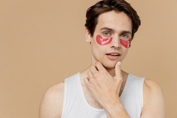 Attractive serious young man 20s perfect skin in undershirt wearing pink patch under eye touch chin...