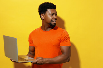Young cool fun student smiling man of African American ethnicity 20s in orange t-shirt hold use...