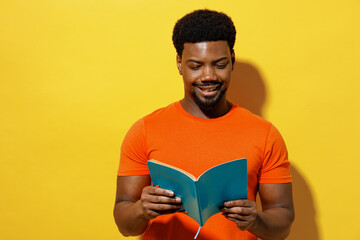 Young smiling student man of African American ethnicity 20s wear orange t-shirt read novel book...