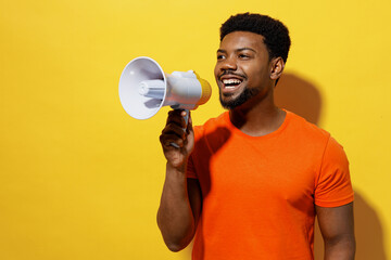 Young man of African American ethnicity 20s wear orange t-shirt hold scream in megaphone announces discounts sale Hurry up isolated on plain yellow background studio portrait People lifestyle concept