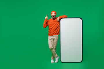 Full body young happy man 20s wear orange sweatshirt hat stand near big blank screen mobile cell...