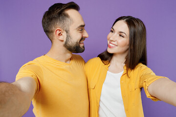 Close up young happy couple two friends family man woman together in yellow casual clothes look to each other do selfie shot pov on mobile phone isolated on plain violet background studio portrait