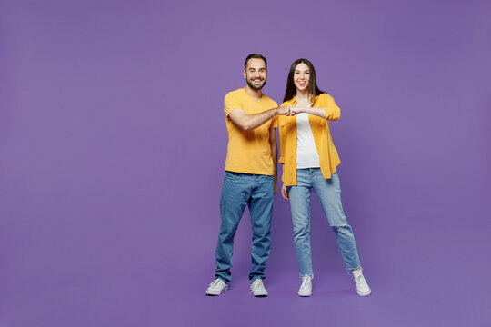 Full body young smiling happy couple two friends family man woman together in yellow casual clothes looking camera giving a fist bump in agreement isolated on plain violet background studio portrait.
