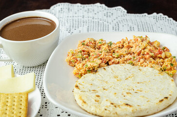 Colombian breakfast. Arepa (ground corn flour dough),egg with traditional sauce called hogado(stir-fried tomato and onion),with cup of chocolate, crackers and cheese,on light background. Close up. 