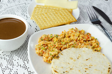 Colombian breakfast. Arepa (ground corn flour dough),egg with traditional sauce called hogado(stir-fried tomato and onion),with cup of chocolate, crackers and cheese,on light background. Close up. 