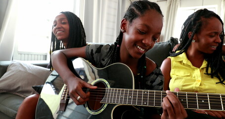 African daughter playing guitar together with family at home sofa