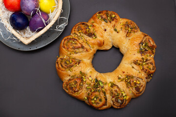 Easter roll with nuts and colored eggs in heart shaped basket. Brown background..
