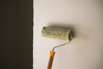 a roller with a yellow handle for applying paint on the wall and an imprint of paint from the roller on the wall.