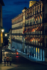 People walking on a Toledo street at night beautifully illuminated by streetlights, shops and the...