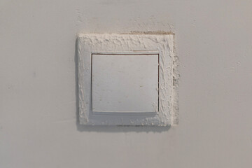 a dirty white light switch on a white wall is damaged and smeared into plaster.