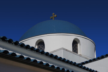 Dome of white Greek Orthodox church with blue roof and blue sky