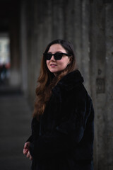 Portrait of a young woman in all-black outfit and black sunglasses. Black clothes, typical Berlin, columns.