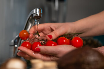Close up female's hands washing homegrown organic red cherry tomatoes with the tap water.