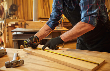 Carpenter working with a wood, marking plank with a pencil and taking measurements to cut a piece...