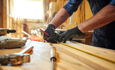 Carpenter working with a wood, marking plank with a pencil and taking measurements to cut a piece of wood to make a piece of furniture in a carpentry workshop, close-up view