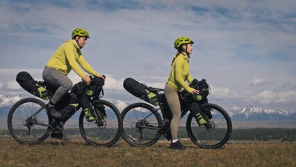 The man and woman travel on mixed terrain cycle touring with bikepacking. The two people journey...