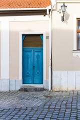 Fototapeta na wymiar Urban architecture background. The exterior wall of house with old lamp and a blue wooden doors on a cobblestone street. Eger, Hungary