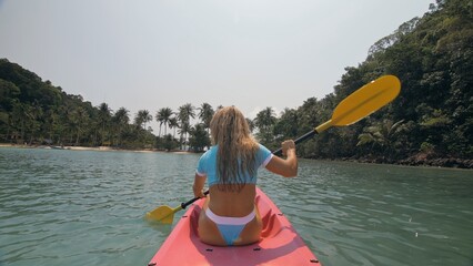 Pretty sexy young blonde woman in stylish swimsuit enjoys trip canoe on sea against palm islands....