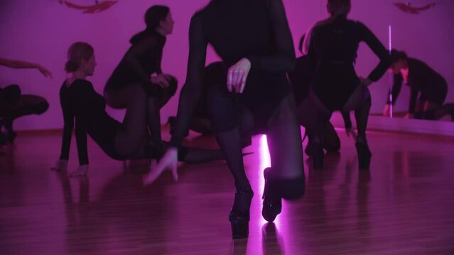 Group of sexy slim women in black clothes preparing for dance workout and one of them performing dancing movements on the floor on foreground