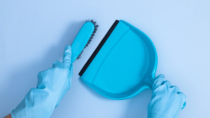 Hands in blue rubber gloves holding broom and fertilizer.on pastel blue background. Cleaning tools and home works concept. Flat lay