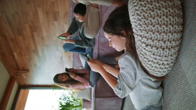 Vertical footage of mother with two little daughters, everyone is using mobile phone in the living room.