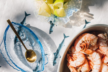grilled prawns on summer evening dinner table with blue fish glass dish and tablecloth, limes, golden spoon
