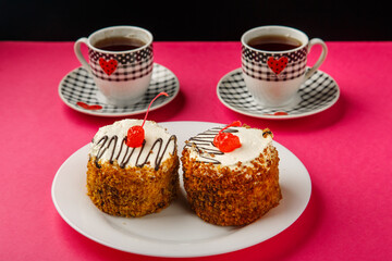 On a pink background, two cups of coffee with hearts and cakes.