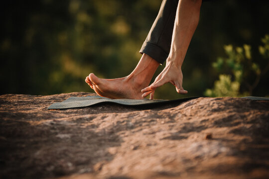 Young man doing yoga at the sunrise on a top of a mountain next the trees over the rocks