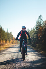Young likeable lady with a lovely realistic smile while recreationally sporting. Cyclist riding fat bike in Finnish wild nature. Vuokatti area. Cycling clothing and helmet