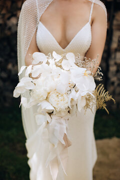 The bride holds in her hands a beautiful wedding bouquet of white orchids and peonies